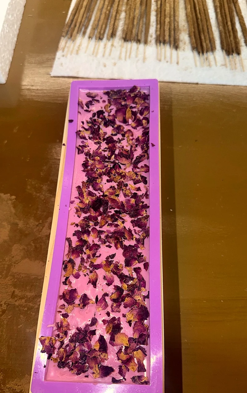 Self Love & Magnetism soap in the mold, topped with dried rose petals, with incense drying behind it.